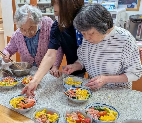 西水元ホームで、入居者さんがスタッフと一緒に料理を盛り付けている様子